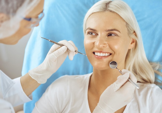 Uśmiechnięta blond kobieta zbadana przez dentystę w klinice dentystycznej. Zdrowe zęby i koncepcja medycyny.