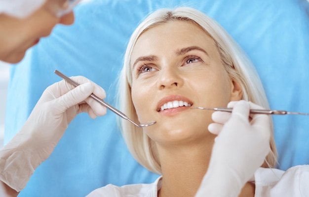 Uśmiechnięta blond kobieta zbadana przez dentystę w klinice dentystycznej. Zdrowe zęby i koncepcja medycyny.
