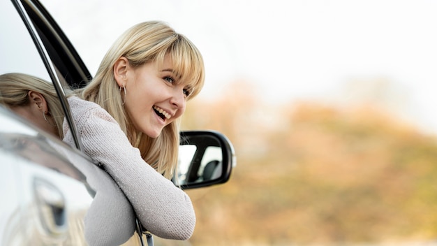 Zdjęcie uśmiechnięta blondynki kobieta bierze jej głowę z nadokiennego samochodu
