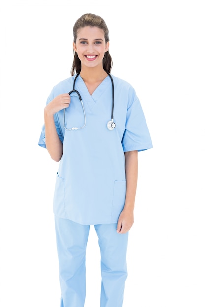 Uśmiechnięta brown z włosami pielęgniarka w błękicie szoruje patrzeć kamerę