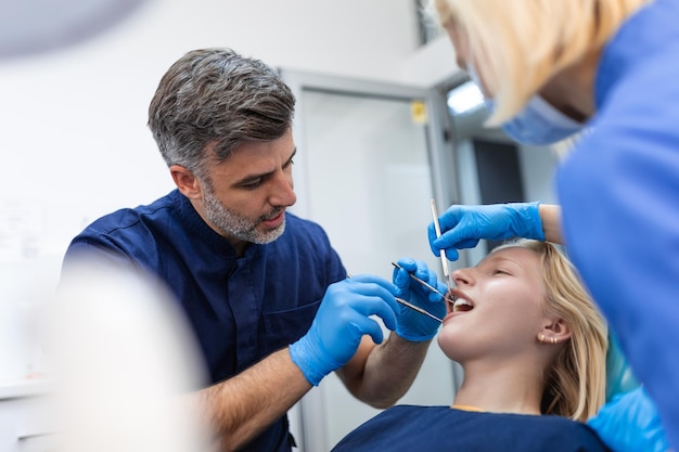 Uśmiechnięta brunetka badana przez dentystę w klinice dentystycznej Ręce lekarza trzymającego instrumenty dentystyczne w pobliżu ust pacjenta Zdrowe zęby i koncepcja medycyny