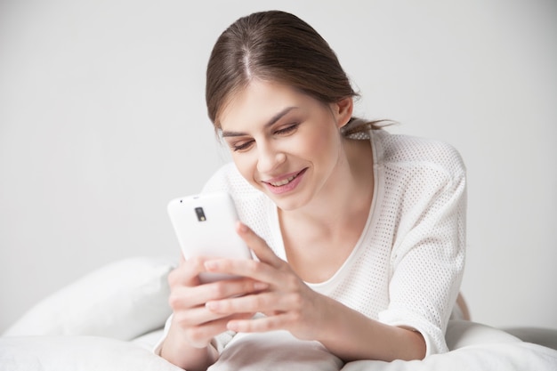 Uśmiechnięta brunetka podczas korzystania ze smartfona na poduszce w domu