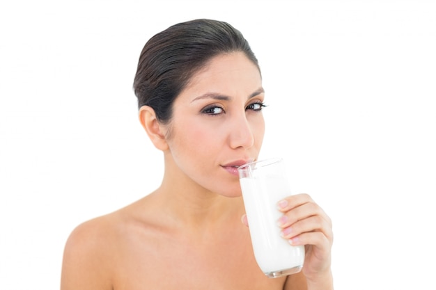Uśmiechnięta brunetka popijając szklankę mleka i patrząc na kamery