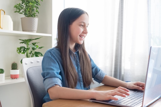 Uśmiechnięta brunetka studiuje przy komputerze w domu, odrabiając pracę domową, komunikując się w sieci