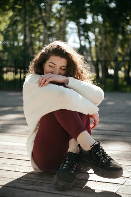 Zdjęcie uśmiechnięta brunetka w białym swetrze siedzi w parku