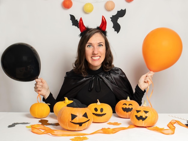 Uśmiechnięta Brunetka W Diabelskim Kostiumie Na Halloween Z Czarno-pomarańczowymi Balonami Na Szarym Tle Koncepcja Halloween