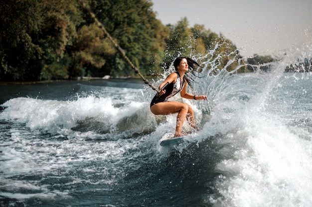 Uśmiechnięta brunetki dziewczyna jedzie na wakeboard trzyma arkanę