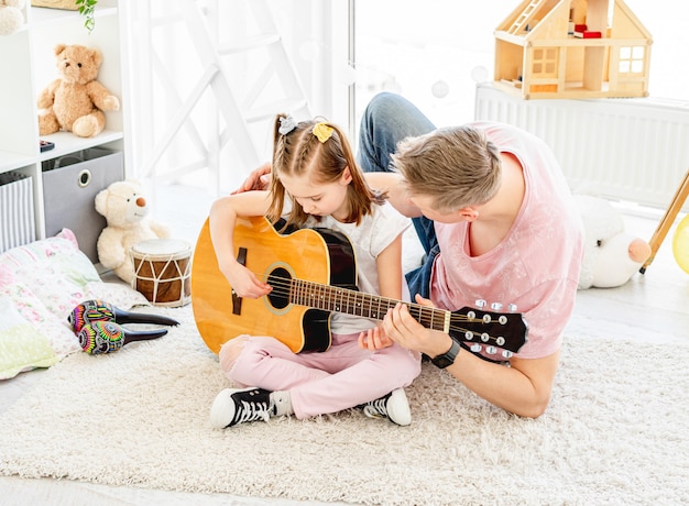 Uśmiechnięta córka z ojcem gra na gitarze