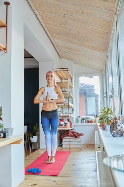 Uśmiechnięta dama trzyma ręce w namaste mudra na balkonie w domu, trening