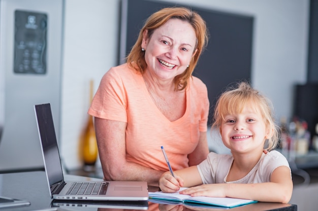 Uśmiechnięta dojrzała mama pomaga córce w przygotowywaniu domowych obowiązków. Koncepcja edukacji online.