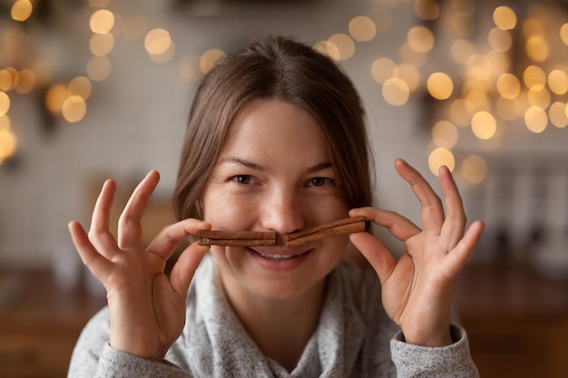 Uśmiechnięta dorosła kobieta robi sztuczne wąsy z laski cynamonu