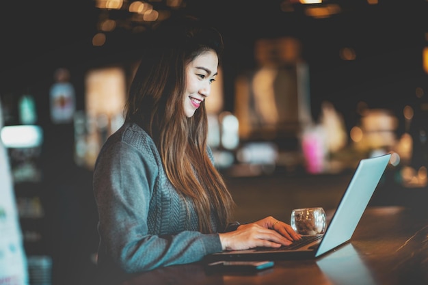 Uśmiechnięta dorosła kobieta używająca laptopa w kawiarni
