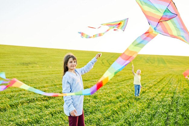 Uśmiechnięta dziewczyna i brat chłopiec biegnący z latającymi kolorowymi latawcami na wysokiej trawiastej łące Szczęśliwe chwile z dzieciństwa