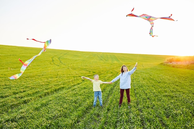 Uśmiechnięta dziewczyna i brat chłopiec stojący i trzymający się za ręce z latającymi kolorowymi latawcami na wysokiej trawie łące Szczęśliwe chwile z dzieciństwa