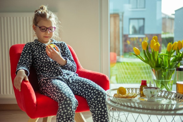 Zdjęcie uśmiechnięta dziewczyna jedząca cytrynę siedząc w fotelu w domu