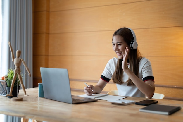 Uśmiechnięta dziewczyna odzież studencka notująca do nauki online z nauczycielem szczęśliwa młoda kobieta ucz się języka słuchaj wykład oglądaj seminarium internetowe pisz notatki patrz na laptopa w domu edukacja na odległość