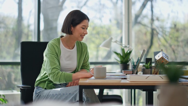 Uśmiechnięta dziewczyna patrząca na ekran laptopa odpoczywająca w miejscu pracy zbliżenie kobieta na przerwie herbaty
