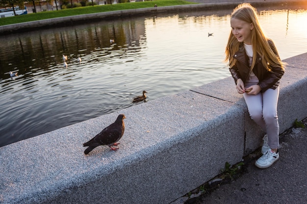 Uśmiechnięta dziewczyna patrząca na ptaka siedząc przy jeziorze podczas zachodu słońca