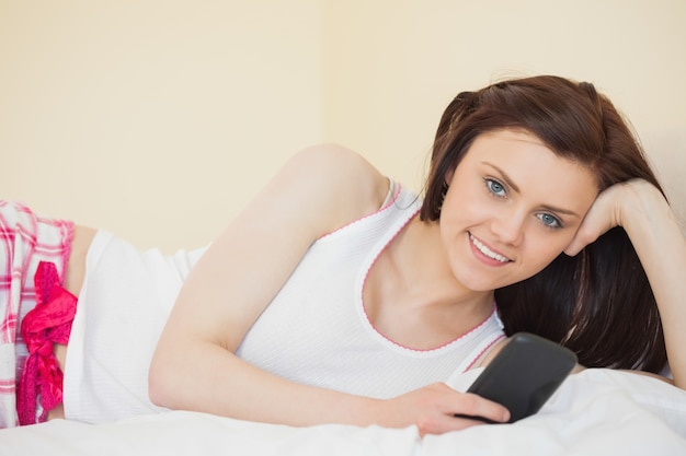 Uśmiechnięta dziewczyna patrzeje kamerę używać jej telefonu lying on the beach na łóżku