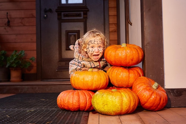 Uśmiechnięta dziewczyna siedzi obok dyń w pobliżu drzwi domu wystrój na halloween Kopiuj przestrzeń