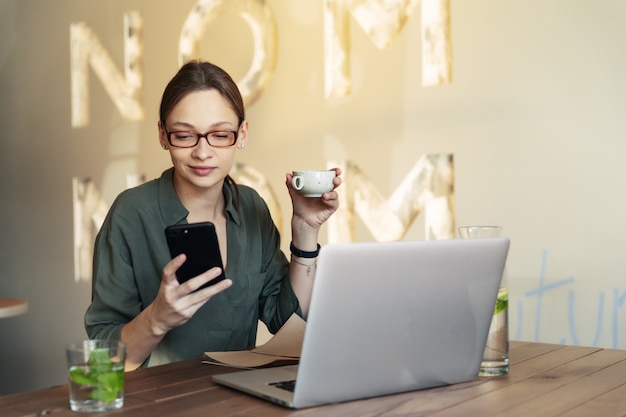 Uśmiechnięta dziewczyna studentka nauki online, szczęśliwa młoda kobieta uczy się języka, pisze notatki, patrzy na laptopa siedzącego w kawiarni, daleka edukacja