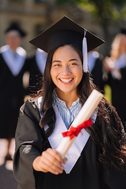 Uśmiechnięta dziewczyna trzyma dyplom i jest dumna ze swojego tytułu magistra