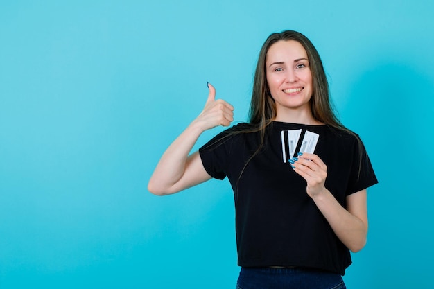 Uśmiechnięta dziewczyna trzyma karty kredytowe i pokazuje doskonały gest na niebieskim tle