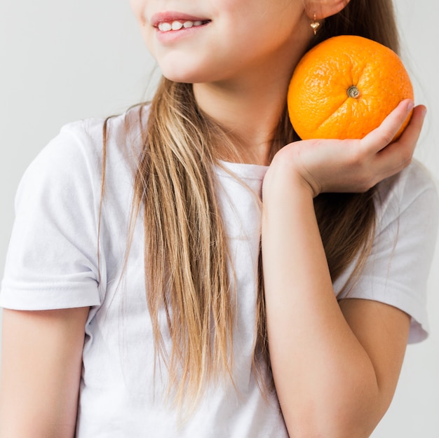 Uśmiechnięta Dziewczyna W Białej Koszulce Trzymając Pomarańczę W Dłoniach. Zdjęcie Pionowe