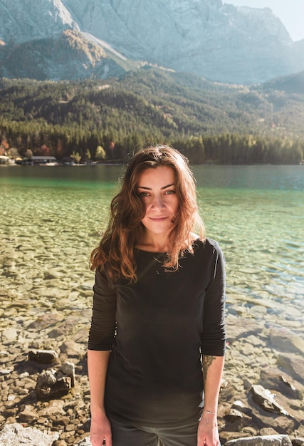 Uśmiechnięta dziewczyna w czarnym swetrze stoi na tle górskiego jeziora Eibsee w