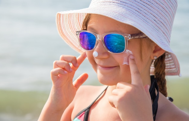 uśmiechnięta dziewczyna w kapeluszu rozmazuje krem ochronny na plaży