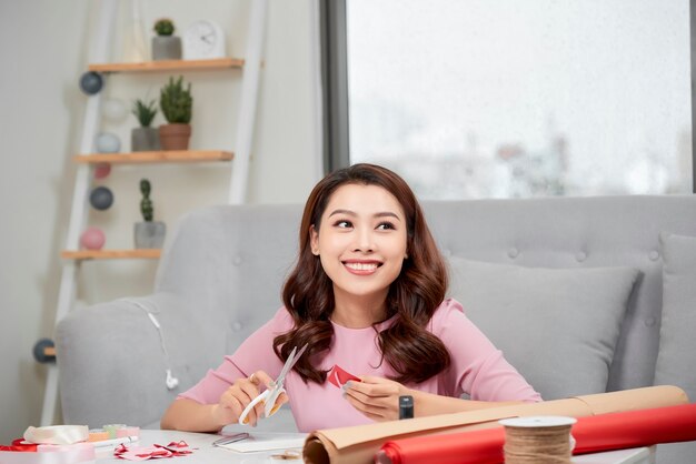 Uśmiechnięta dziewczyna wycinająca walentynkowe serce z czerwonego papieru nożyczkami w salonie
