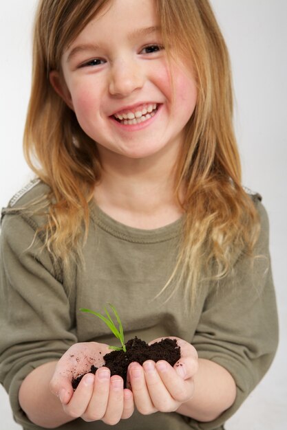 Uśmiechnięta dziewczyna z rośliny dorośnięciem od ziemi w rękach