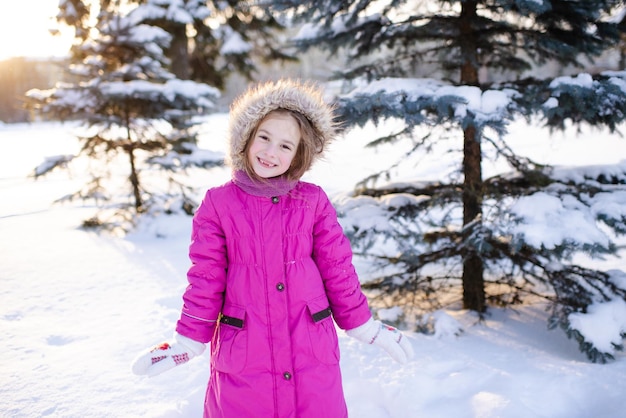 Uśmiechnięta dziewczynka 5-6 lat nosić różową kurtkę zimową w snowy parku na zewnątrz. Patrząc na aparat. Dzieciństwo.