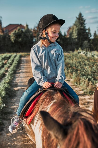 Zdjęcie uśmiechnięta dziewczynka ucząca się jeździć konno 5-6 letnia jeździecka w hełmie