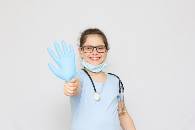 Uśmiechnięta Dziewczynka W Mundurze Medycznym I Niebieskich Rękawiczkach Patrząca Na Kamerę Na Białym Tle