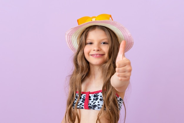 Zdjęcie uśmiechnięta dziewczynka w stroju kąpielowym na odosobnionym tle daje kciuki do góry.