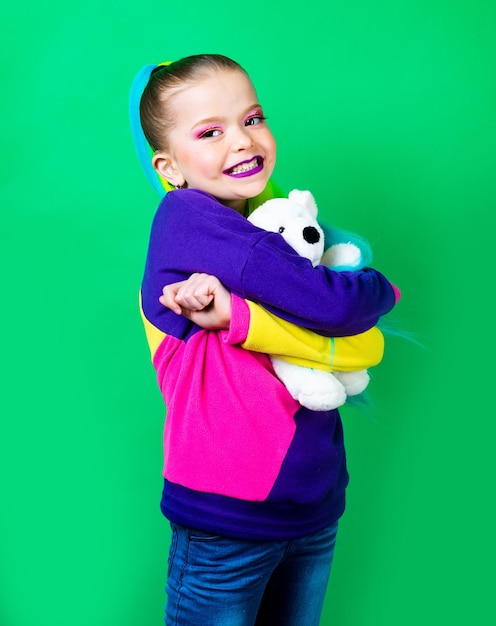 Uśmiechnięta dziewczynka z kolorowymi włosami obejmująca pluszowego misia Koncepcja przystawek dla dzieciZabawki wrażliwe na tekstylia