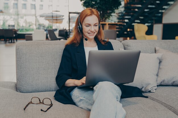 Uśmiechnięta Freelancerka Nosząca Bezprzewodowy Zestaw Słuchawkowy Komunikująca Się Z Klientem Za Pośrednictwem Połączenia Wideo Na Laptopie