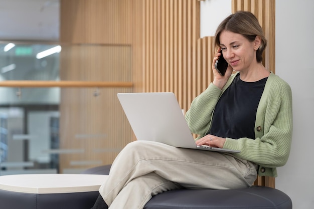 Uśmiechnięta freelancerka w średnim wieku, pracująca zdalnie na laptopie, wykonująca telefon do klienta