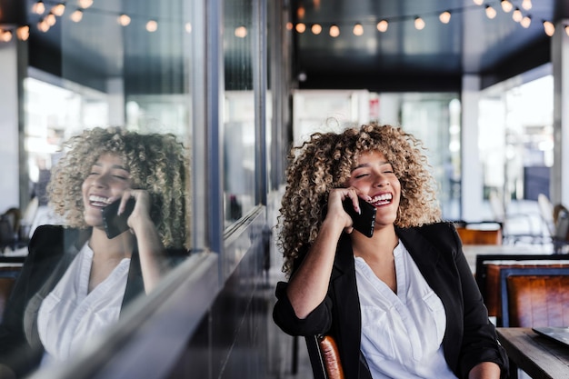 Uśmiechnięta hiszpańska afro kobieta biznesowa w kawiarni pracująca na laptopie i telefonie komórkowym biznes lifestyle