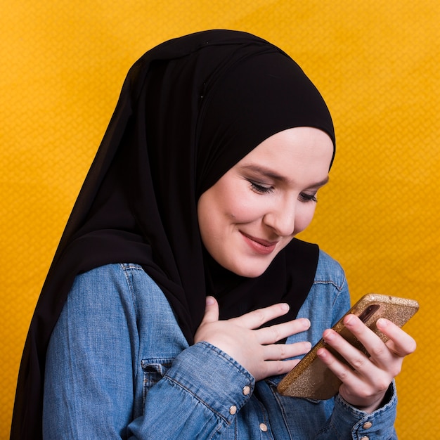 Uśmiechnięta islamska kobieta patrzeje jej telefon z chustka na głowę