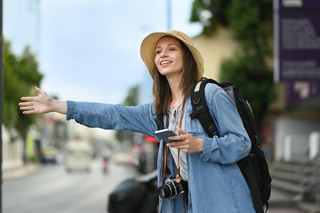 Zdjęcie uśmiechnięta kaukaska podróżniczka podnosząca rękę wzywająca taksówkę na ruchliwej ulicy miasta koncepcja turystyki i transportu