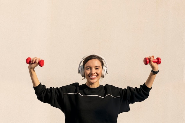 Uśmiechnięta kaukaska tysiącletnia dama w słuchawkach sportowych wykonująca ćwiczenia z hantlami ręcznymi