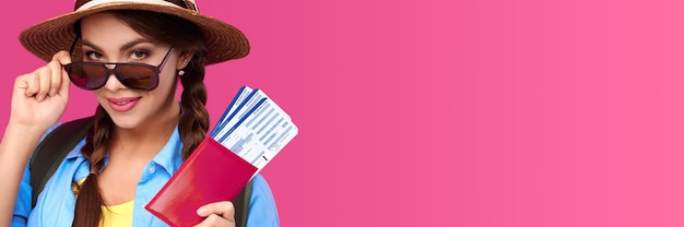 Zdjęcie uśmiechnięta kaukaski kobieta w okularach przeciwsłonecznych trzyma paszport z biletem podróżnym wewnątrz na różowym tle izolowania. strzał studoi
