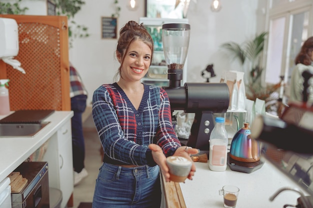 Uśmiechnięta kobieta barista trzymająca filiżankę cappuccino