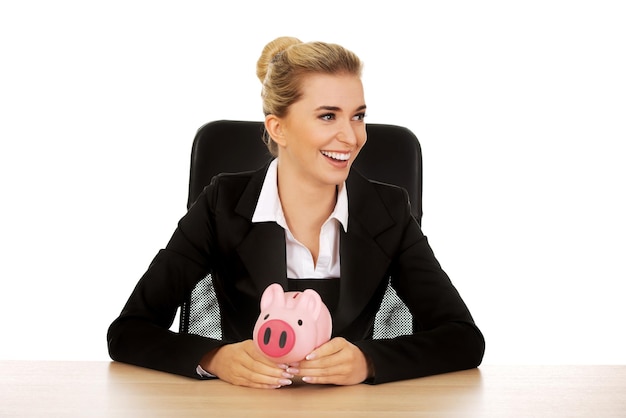 Zdjęcie uśmiechnięta kobieta biznesowa trzymająca świnię, siedząc na krześle na białym tle