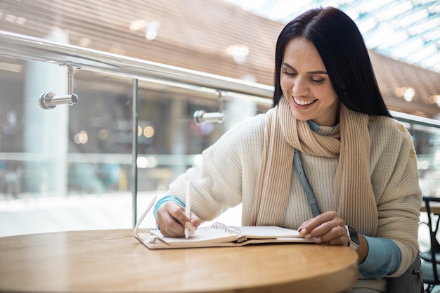 Uśmiechnięta kobieta biznesu pisząca papierową listę robiącą notatki w centrum handlowym o pozytywnych emocjach