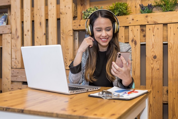 Uśmiechnięta kobieta czytająca wiadomość na smartfonie podczas pracy na laptopie