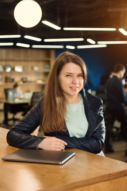 Uśmiechnięta Kobieta Freelancer Pracująca W Przestrzeni Coworkingowej Lub Twórczej, Siedząca Obok Laptopa Nad Grupą Ludzi