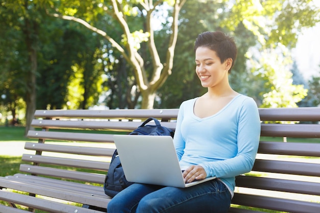 Uśmiechnięta kobieta freelancer z laptopem na zewnątrz. Szczęśliwa dziewczyna pisania na komputerze. Koncepcja technologii, komunikacji, edukacji i pracy zdalnej, kopia przestrzeń